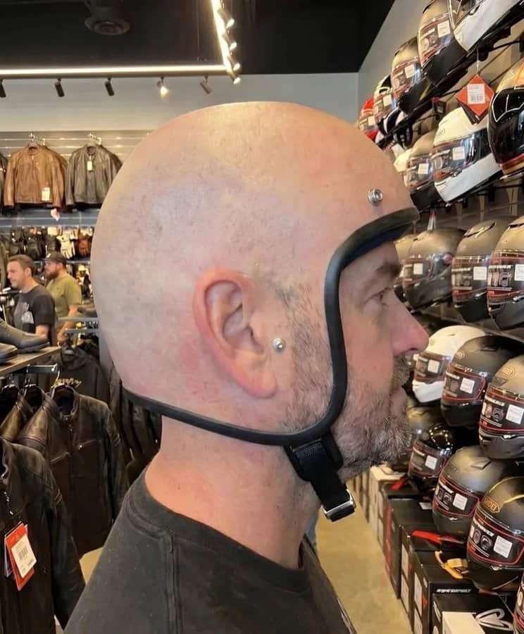 Man wearing a helmet with a bald head in a store with helmets on shelves.