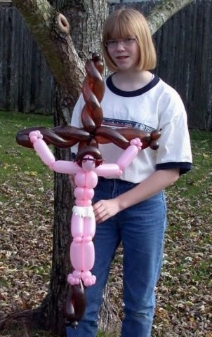 Girl holding a balloon sculpture resembling a muscular figure with a tree in the background.