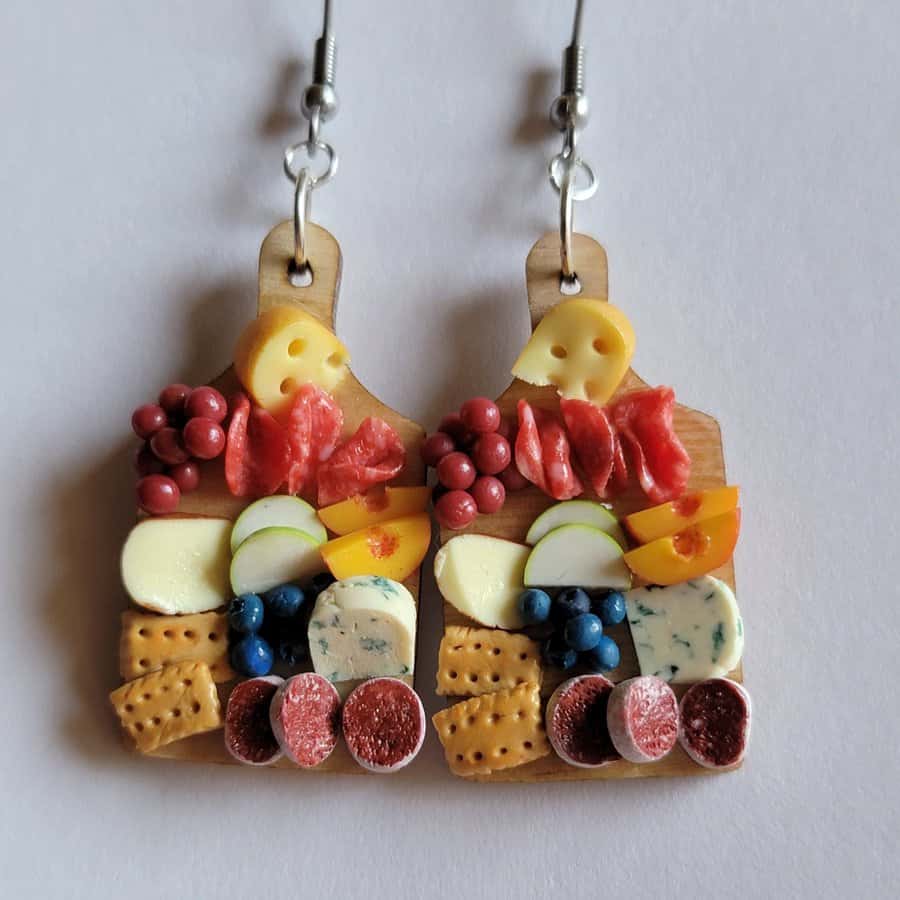 Earrings made of miniature cheese, meat, and fruit slices on wooden bases.