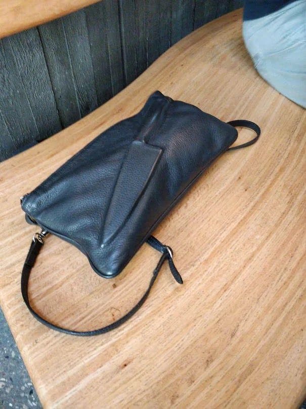 Black leather clutch bag with wrist strap on wooden table.