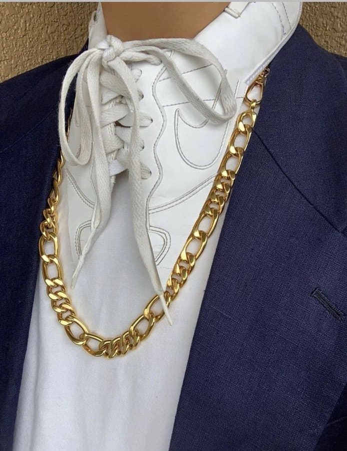 White sneaker, gold chain, navy blazer, and white shirt with text.