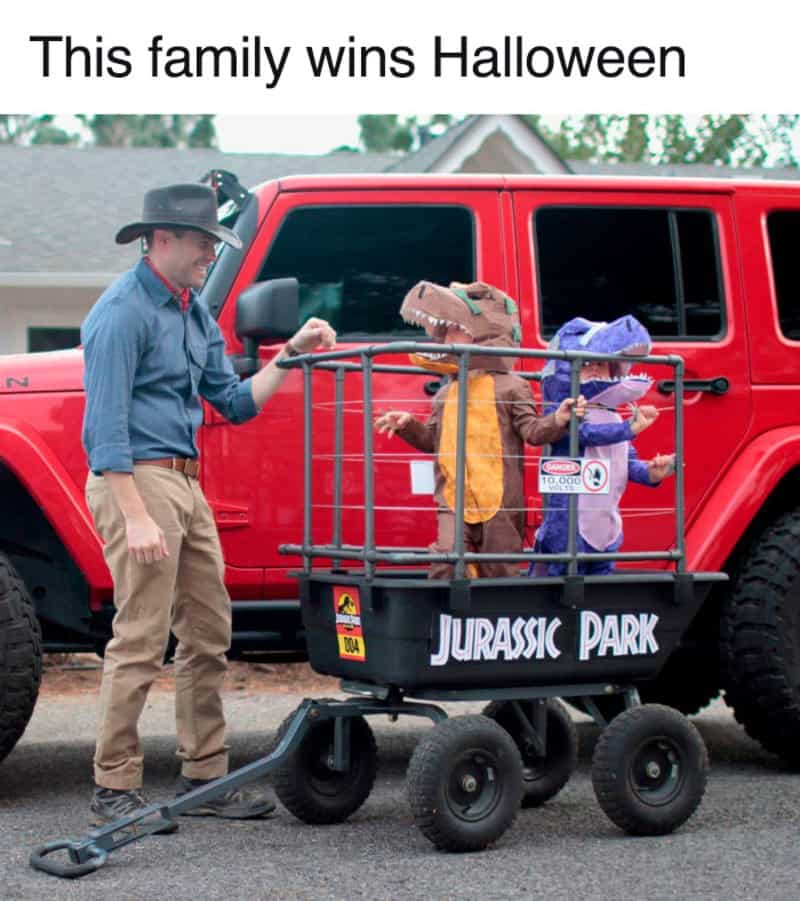 Family in dinosaur costumes with Jurassic Park cart in front of a red truck.