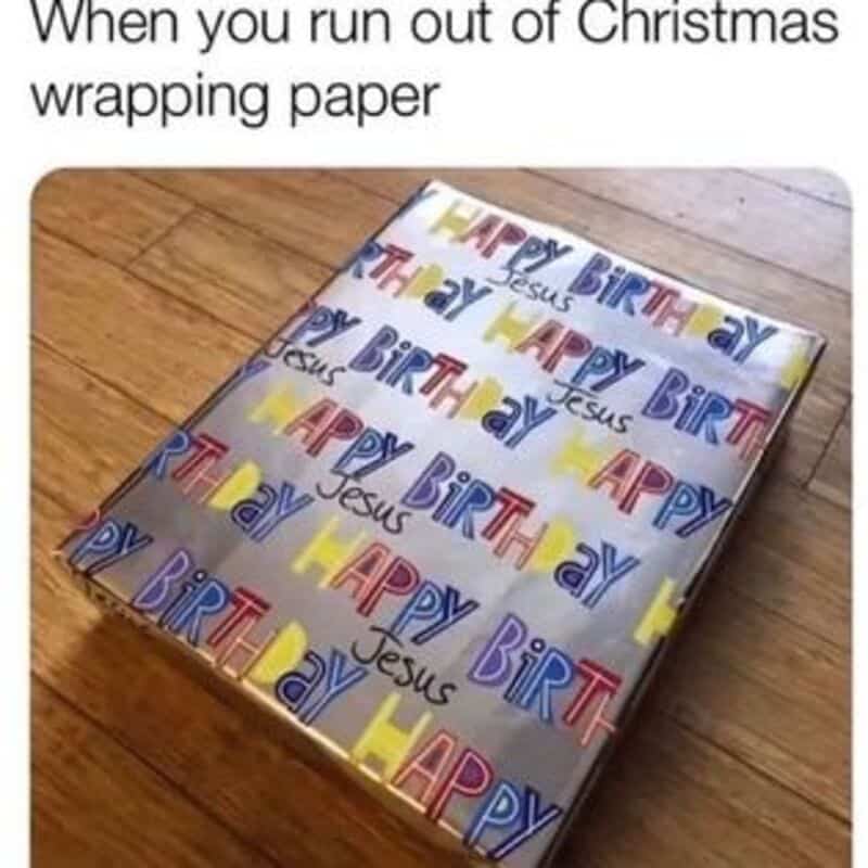 Gift wrapped with colorful 'Happy Birthday Jesus' paper, on a wooden surface.