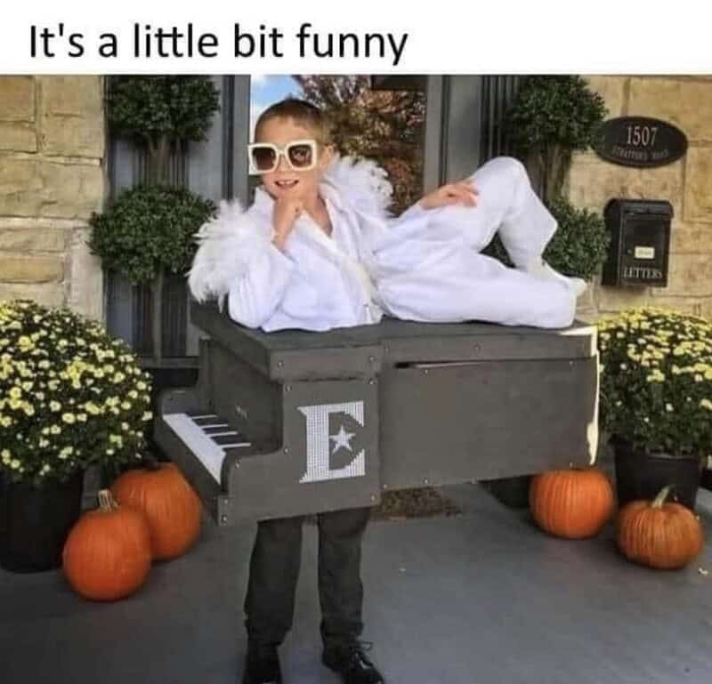 Child in white costume with sunglasses lying on a piano prop outside with pumpkins.
