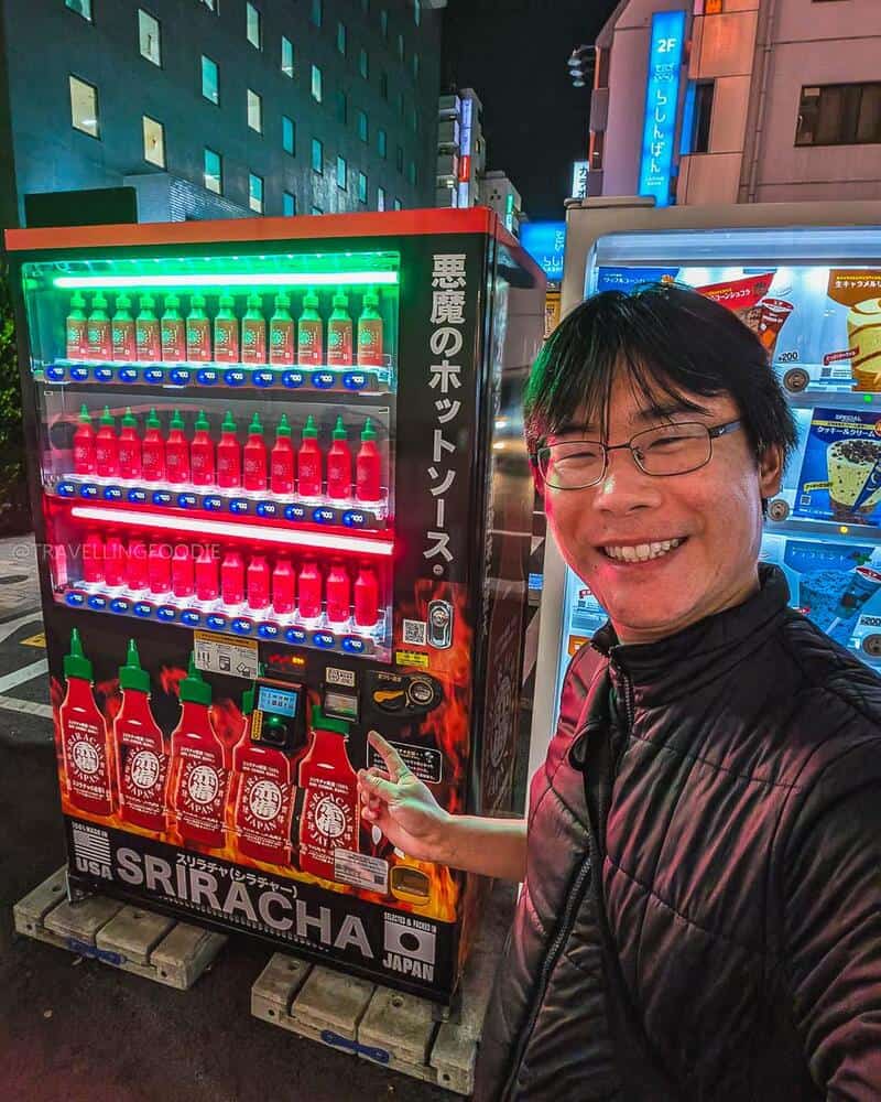 Person smiling at vending machine with hot sauces in an urban setting at night.