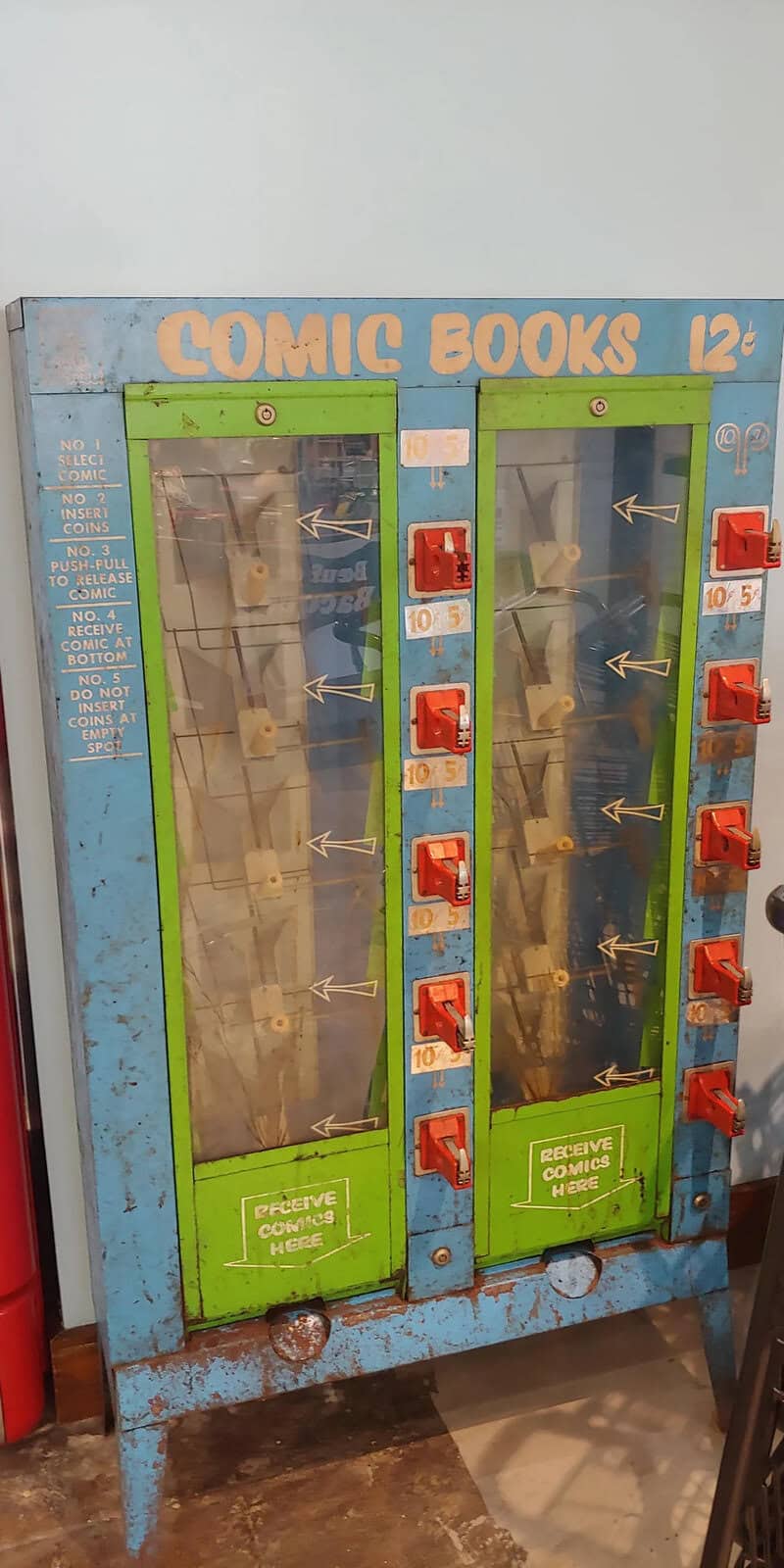 Vintage comic book vending machine with glass doors and red coin slots.