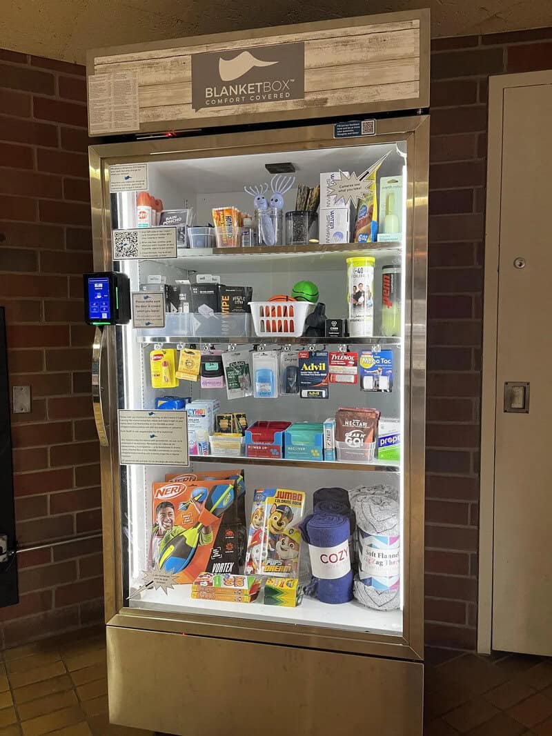 Vending machine with various snacks and drinks, located against a brick wall.