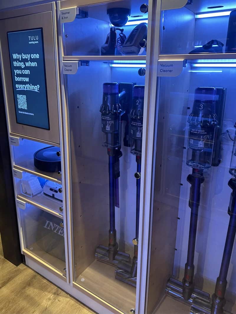Vending machines with vacuum cleaners inside, illuminated by blue light.
