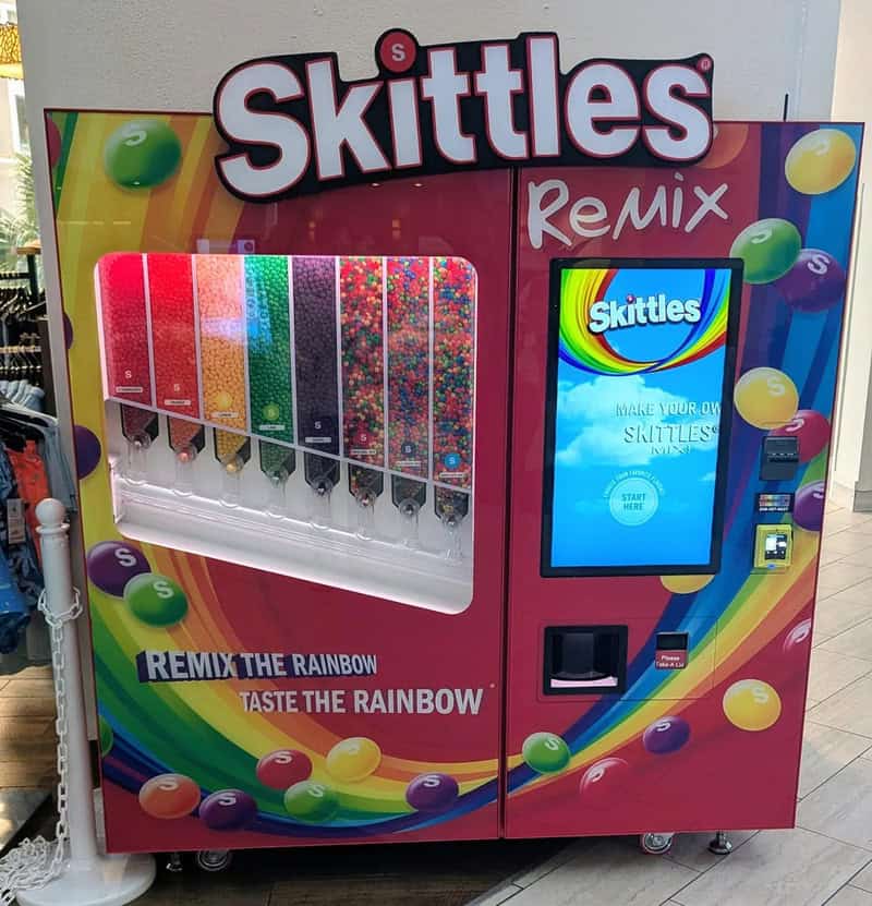 Skittles Remix vending machine with rainbow colors and a digital screen.