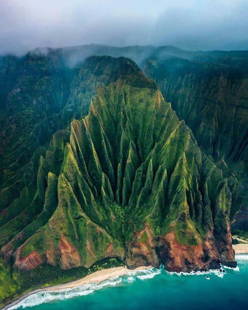 Aerial view of lush green mountains and a coastline with waves crashing.