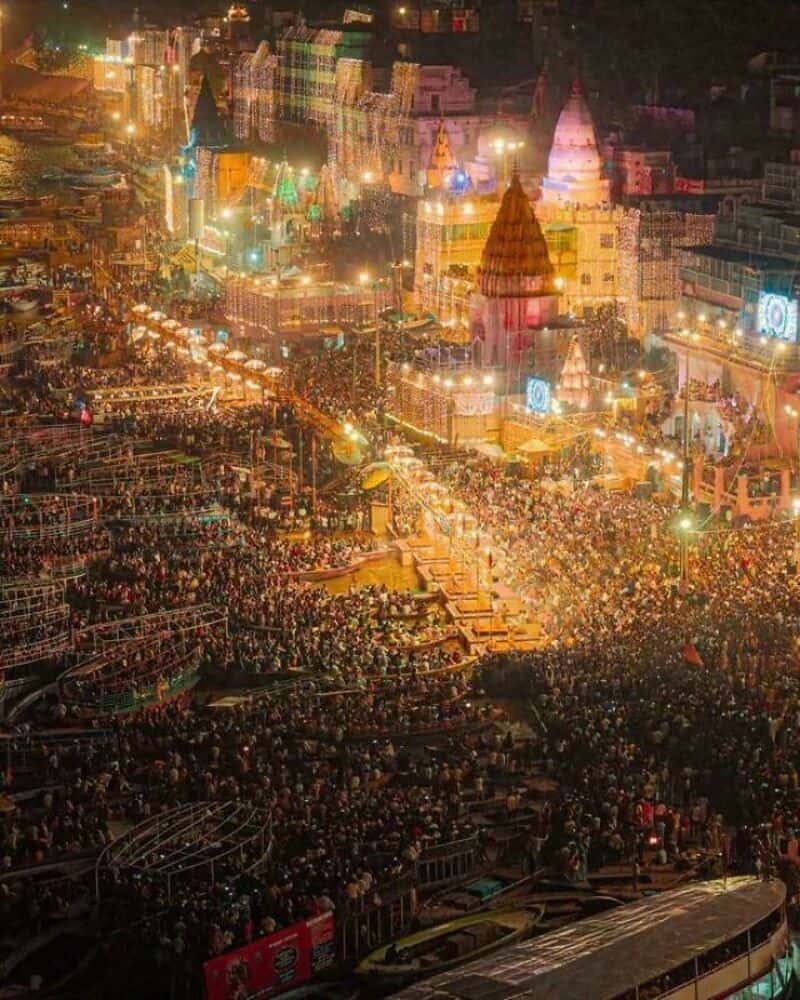 Large crowd at a festival with illuminated temples and colorful lights.