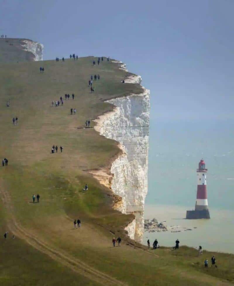 Cliffs with people walking and a lighthouse in the distance.
