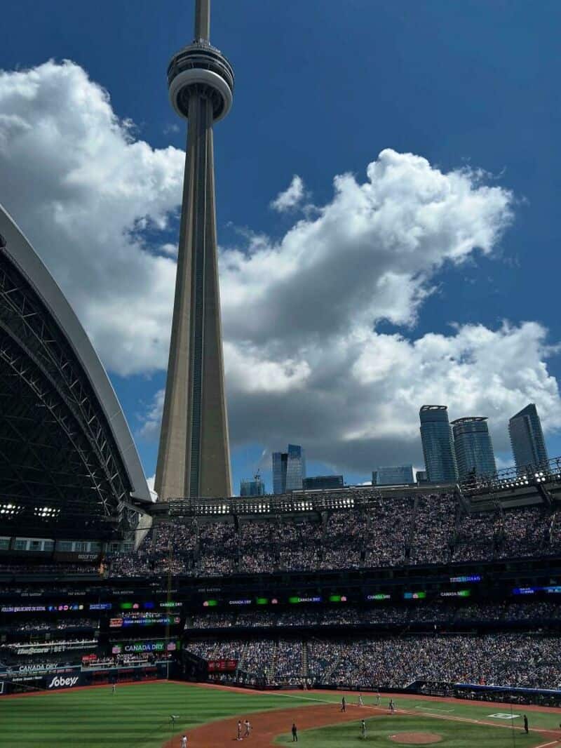 CN Tower towering over a stadium with a crowd and blue sky with clouds.