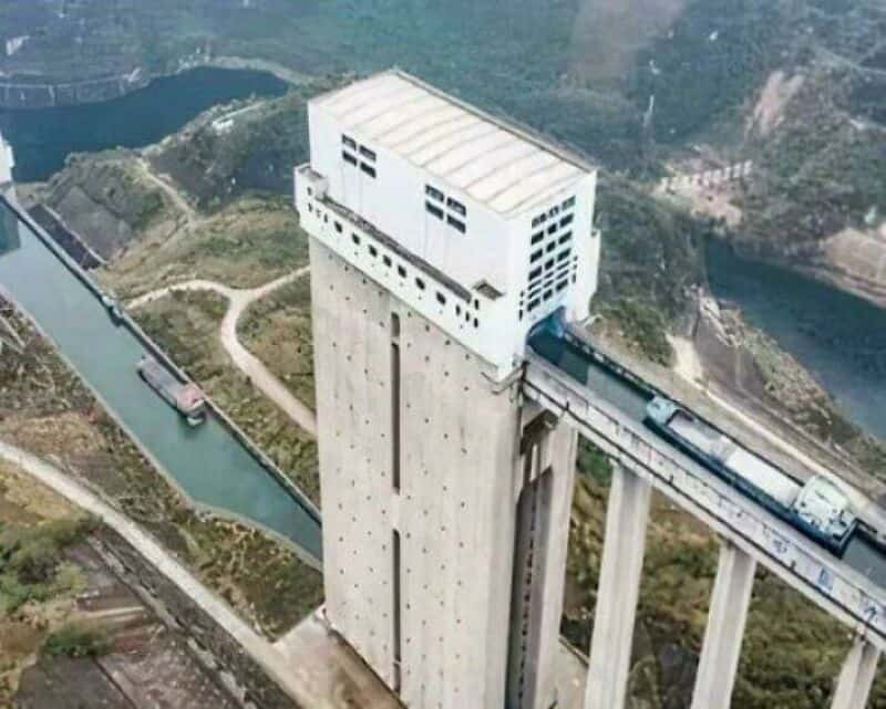 Large dam with a building on top and a train passing through a tunnel.