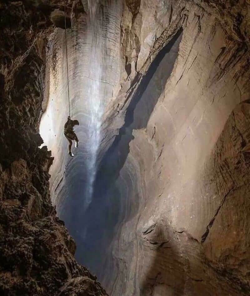Climber descending into a deep, narrow cave with towering walls.