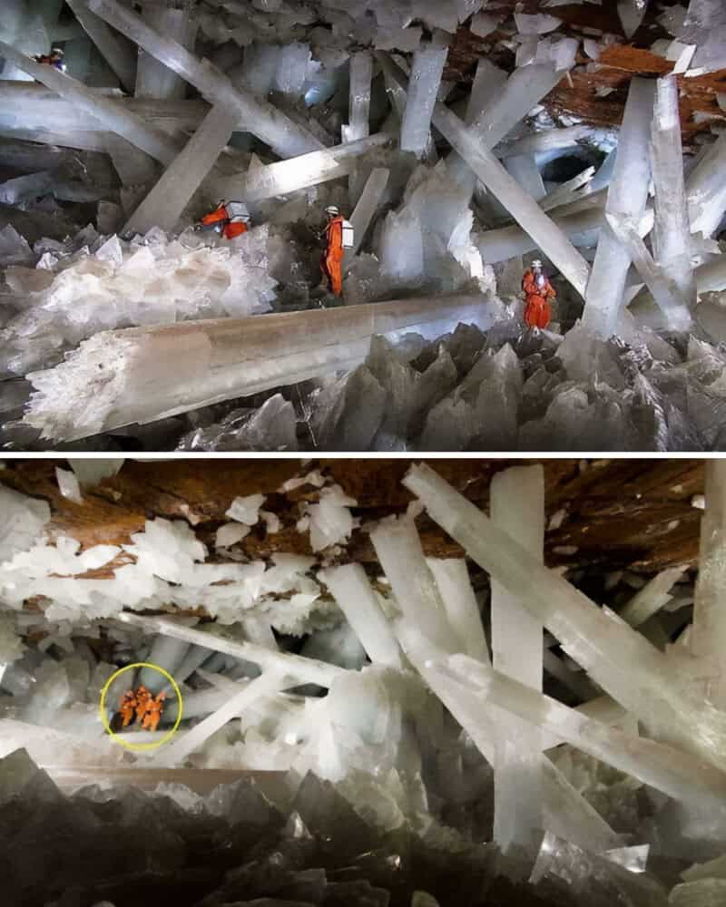 Two workers in orange suits explore a large ice cave with massive ice formations.