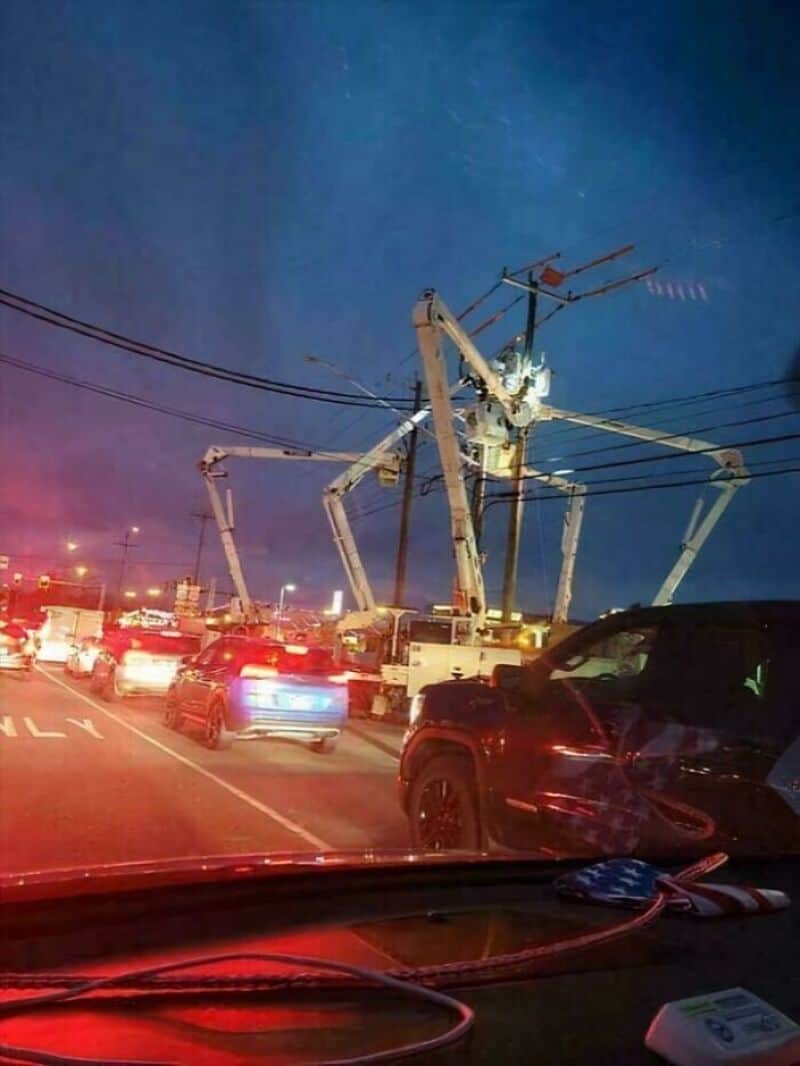 Large mechanical spider on power pole during night with cars in traffic.