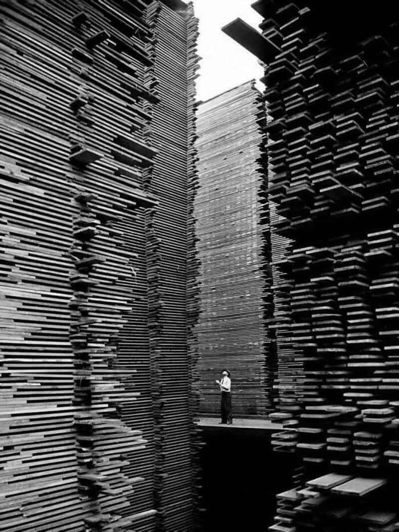 A person standing between towering stacks of books in black and white.