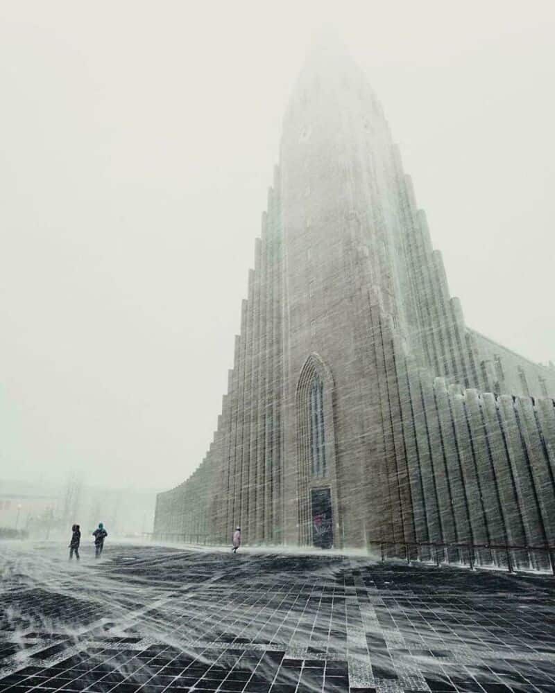 Tall, foggy skyscraper with people at its base in a cityscape.