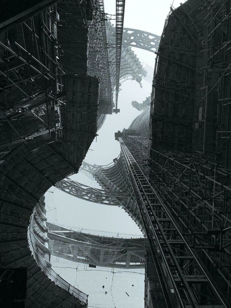 Looking up at a massive, complex construction site with towering steel structures and scaffolding.