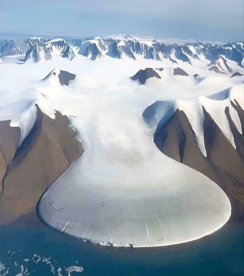 Massive glacier surrounded by snow-capped mountains under a cloudy sky.