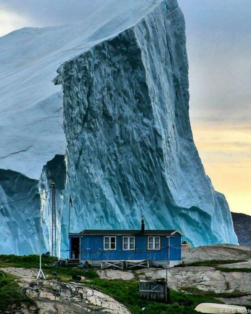 A small blue house in front of a massive ice formation or glacier.