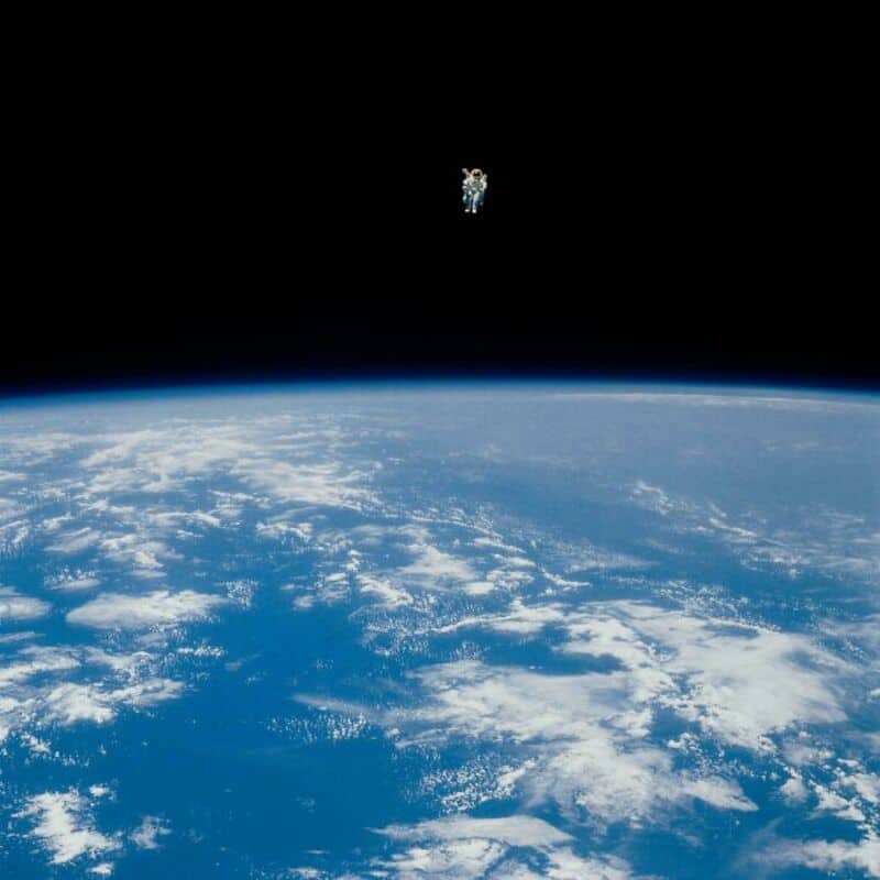 Astronaut floating above Earth with space and planet's atmosphere in the background.
