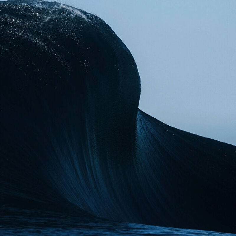 A large ocean wave curling over with dark blue water and white spray at the top.