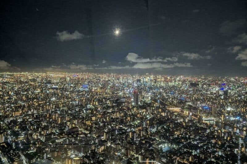 Night cityscape with bright lights and a full moon in the sky.