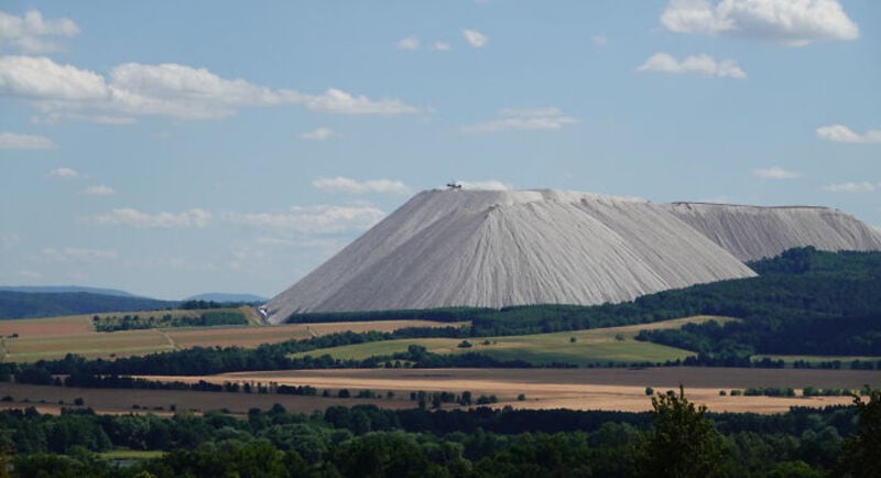 Large white mountain or hill with a flat top, surrounded by green fields and blue sky.