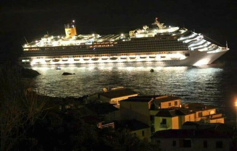 Large cruise ship illuminated at night near a small town.