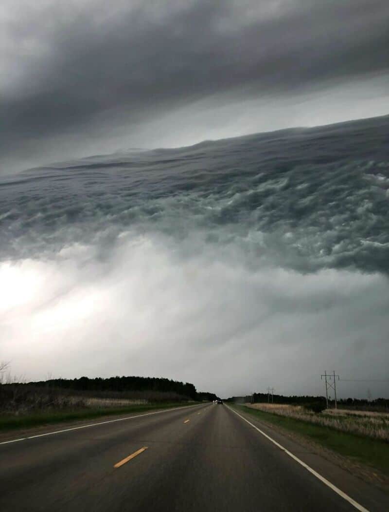 Stormy sky with massive, swirling cloud formation over a road.