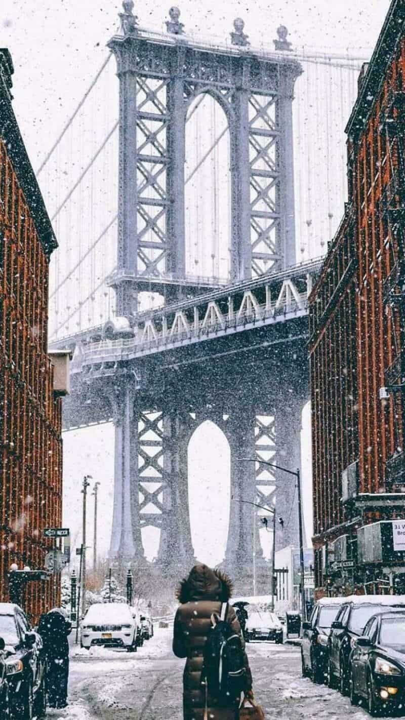 View of a large suspension bridge seen from a snowy street with cars and pedestrians.