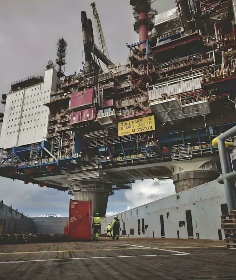 Large offshore oil platform with workers below, under a cloudy sky.