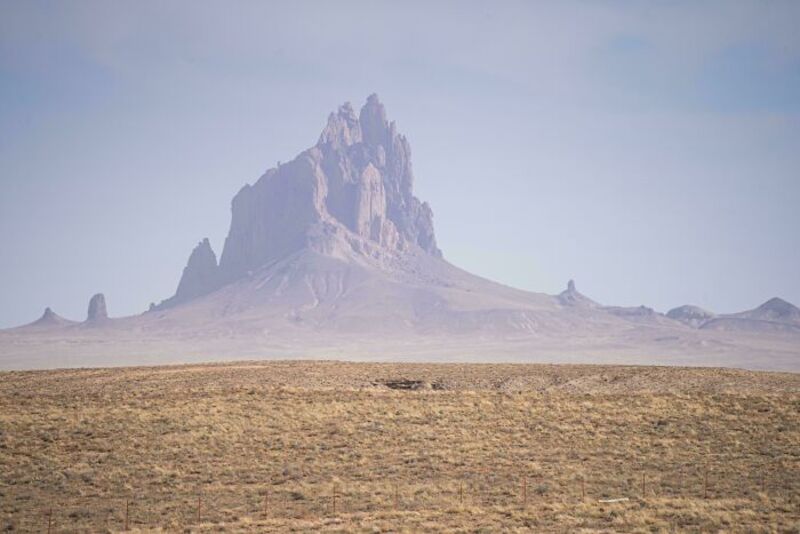 Large mountain formation rising from flat terrain under cloudy sky.