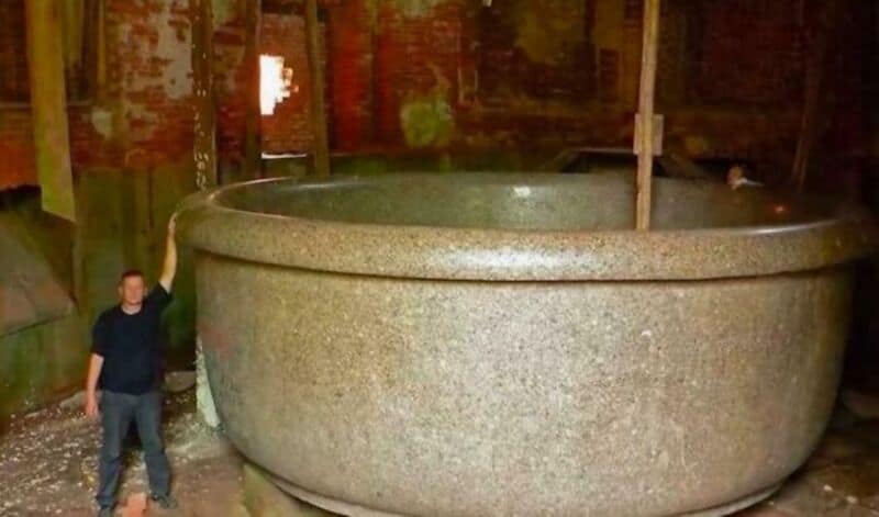 Person standing next to a giant stone bowl in a rustic setting.