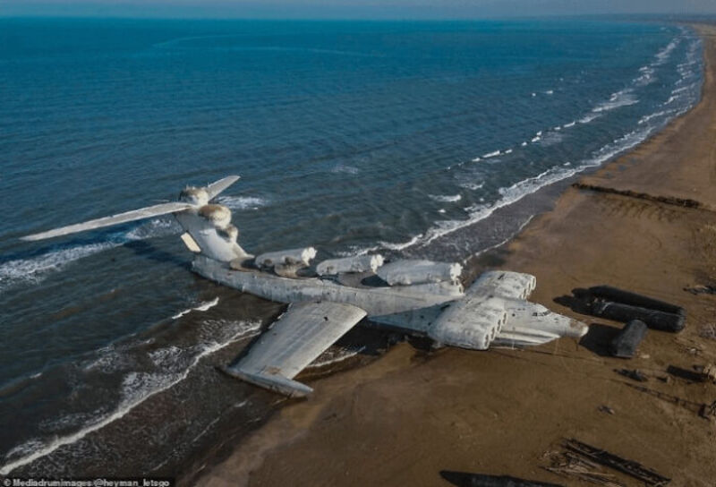 Large crashed aircraft on beach, wings and tail damaged, near water.