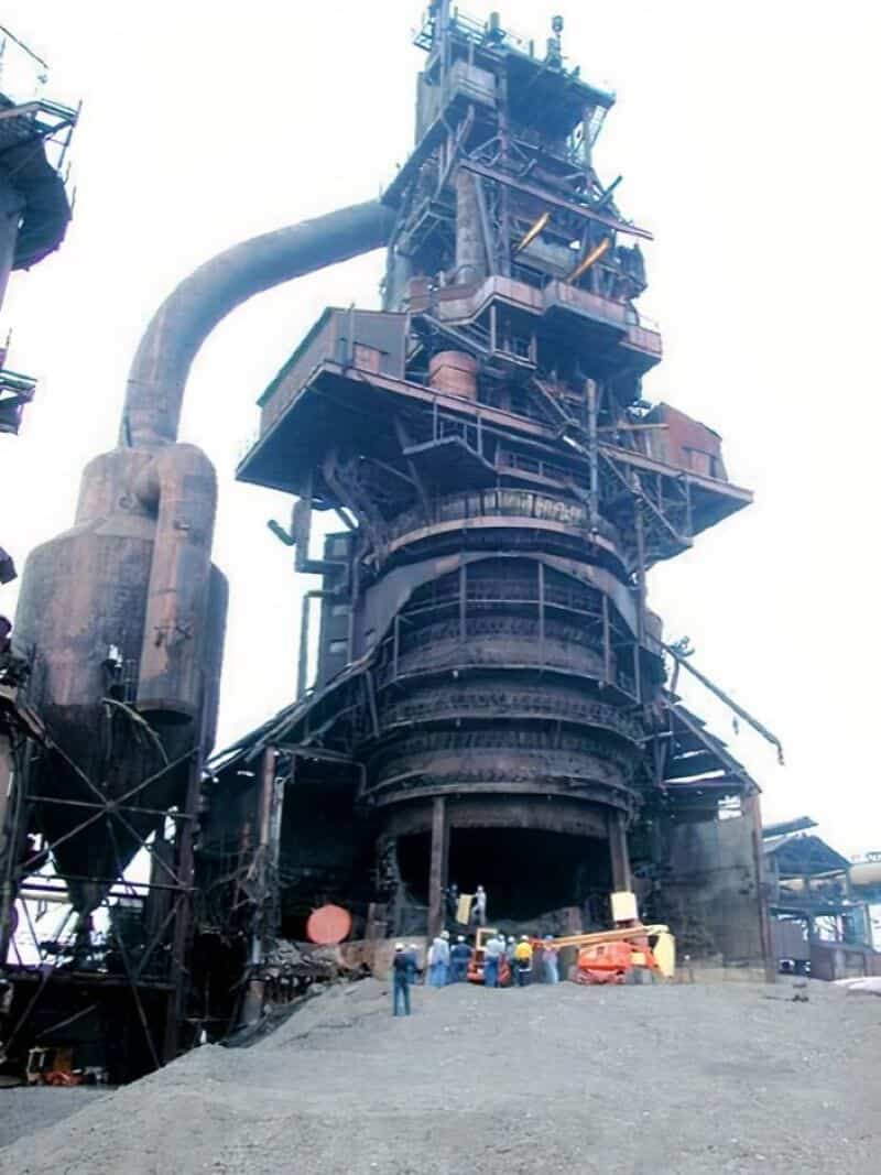 Large industrial factory with towering structures and pipes, under a clear sky.