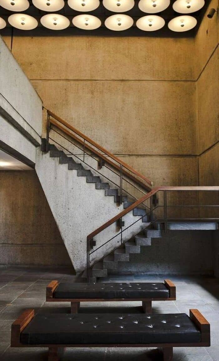 Concrete staircase with wooden handrails and modern lighting fixtures above.