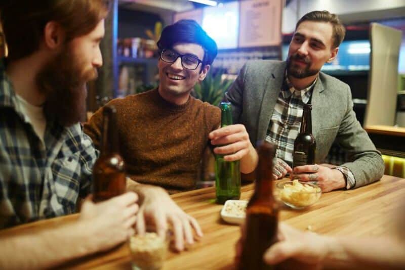 Three men enjoying drinks and snacks at a bar, smiling and talking.