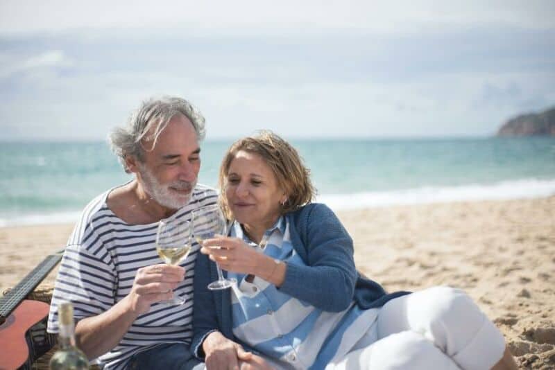 Older couple enjoying wine on the beach with ocean in the background.