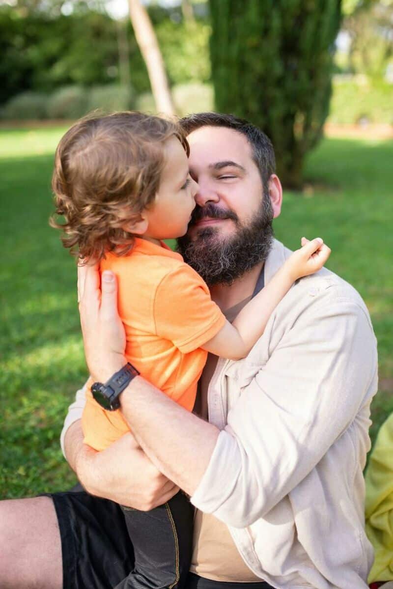 Father and son sharing a kiss outdoors in a park.