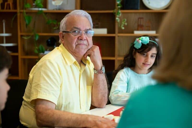 Elderly man with glasses and yellow shirt sitting at a table with a young girl.