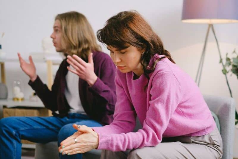 Two women sitting on a sofa, one appears upset, the other is talking.