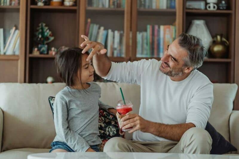 Grandfather playing with granddaughter, smiling, in living room.