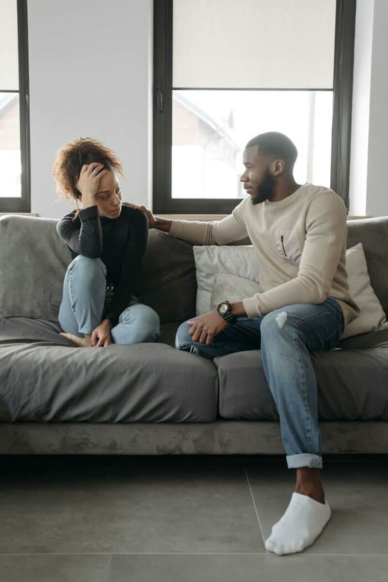 A man comforts a distressed woman sitting on a sofa in a modern living room.