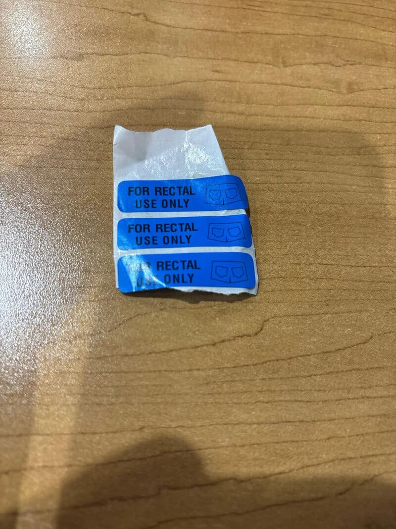 Small crumpled paper with blue labels reading 'FOR RECTAL USE ONLY' on a wooden surface.