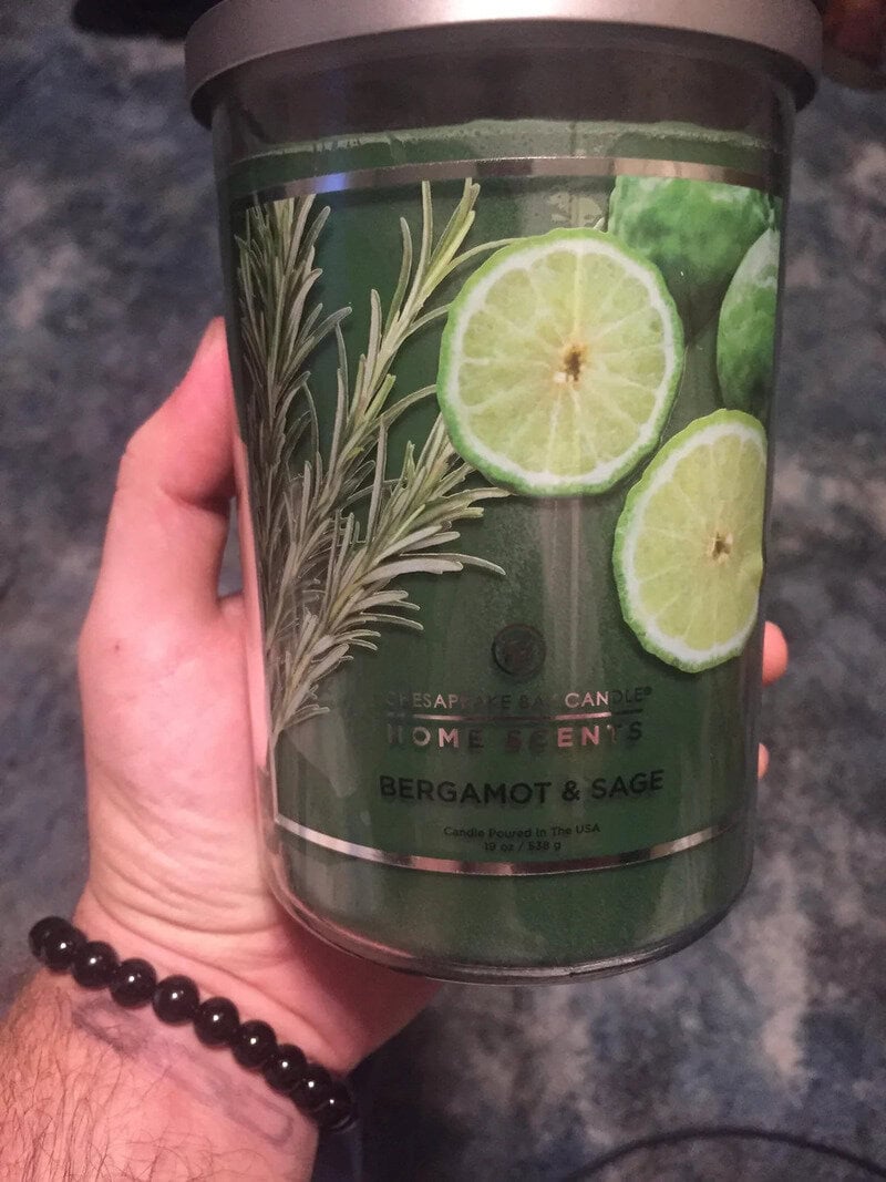 Candle with bergamot and sage scent, featuring lemon slices and herbs on label.