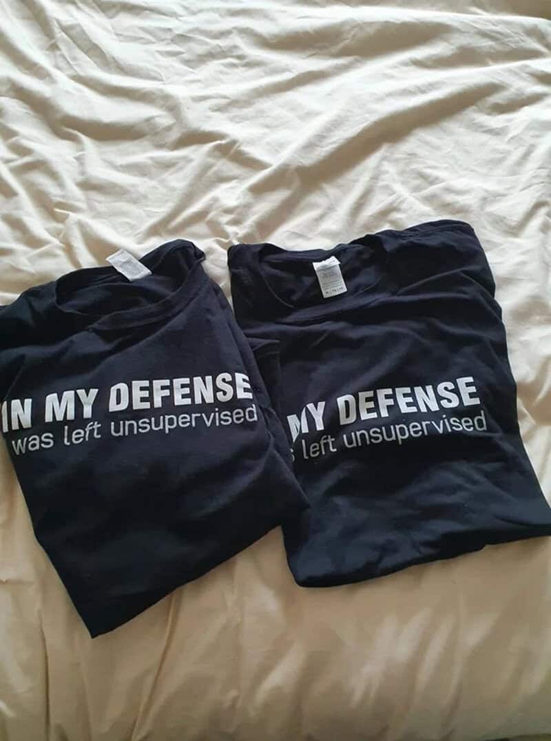 Two black T-shirts with white text on a beige bedspread.