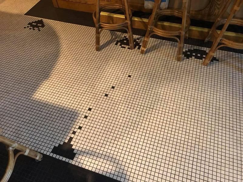 Mosaic floor with a black and white pattern and wooden chairs along the wall.